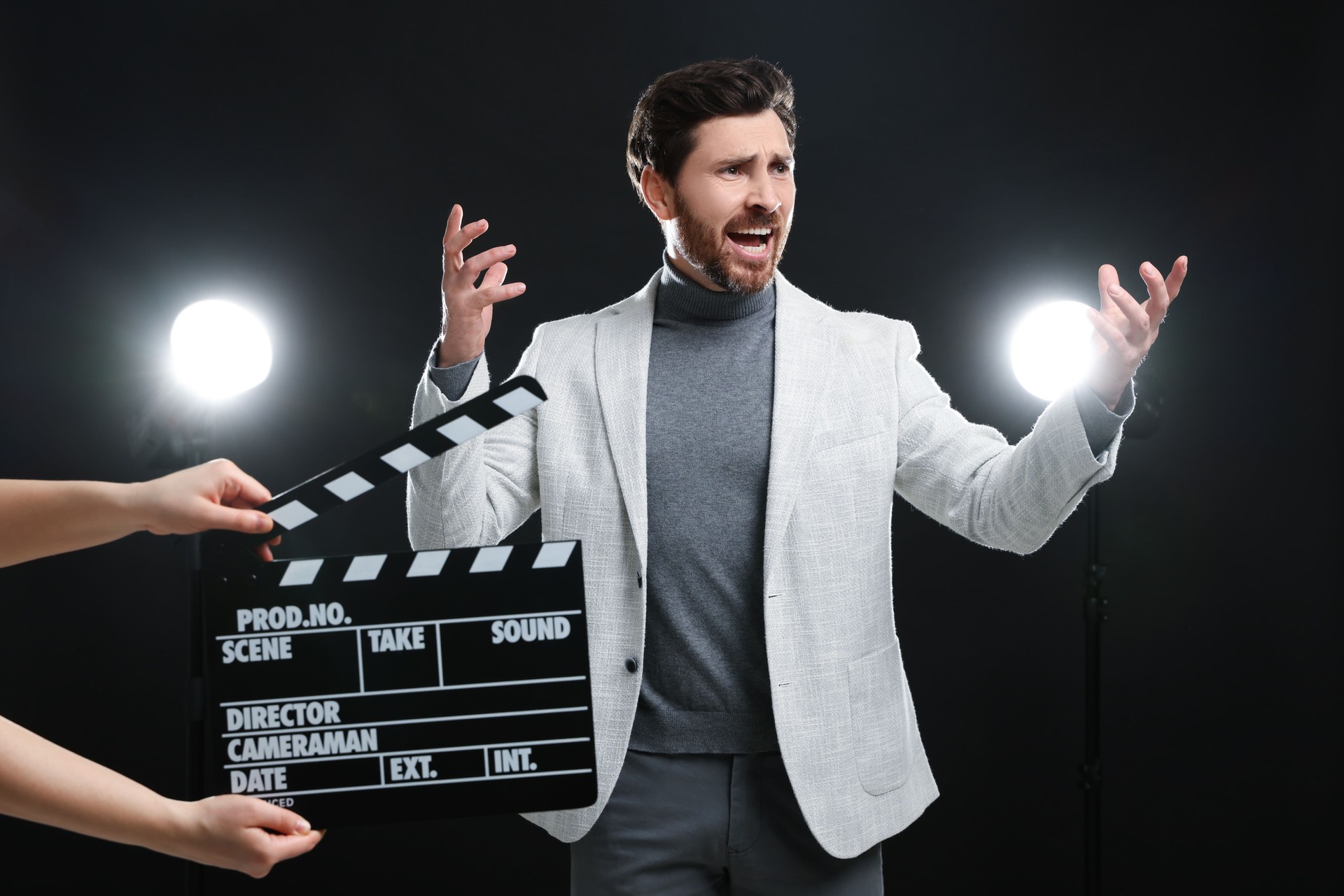 Emotional actor performing while second assistant camera holding clapperboard on black background
